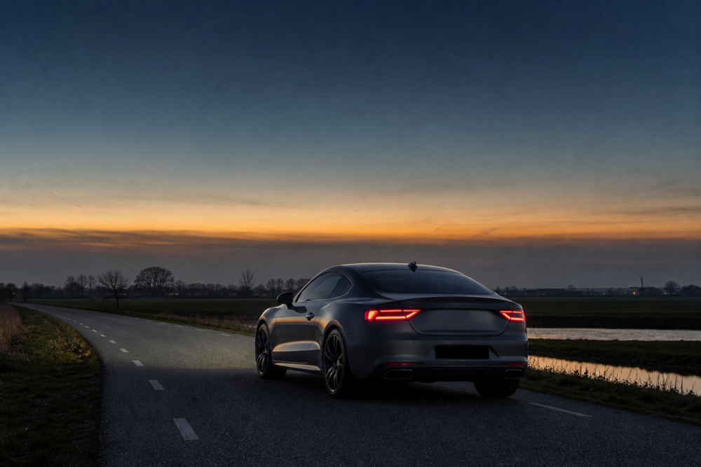 Donkere performance coupé op een rustige landelijke weg bij zonsondergang.